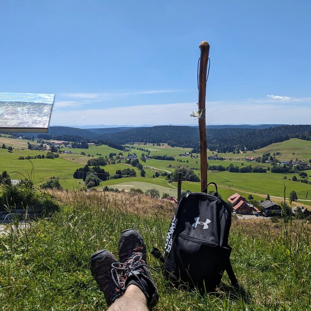 A person sits on a grassy hill, backpack beside them, studying a map under a clear blue sky.