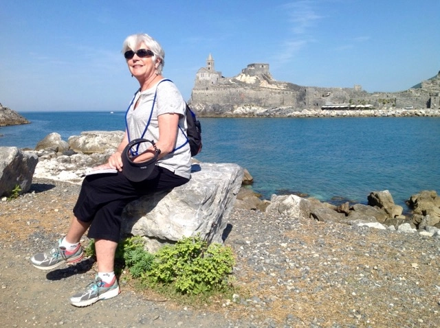 An older woman relaxes on a rock by the ocean, enjoying the serene view and gentle waves lapping at the shore.