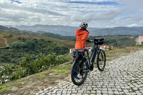 Woman in orange jacket looks out over bike in Portugal