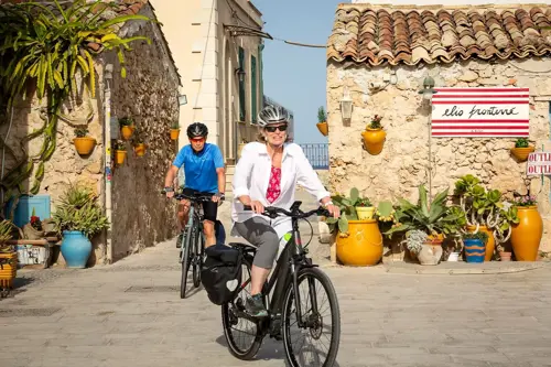 Older man and woman ride bikes in Sicily, Italy