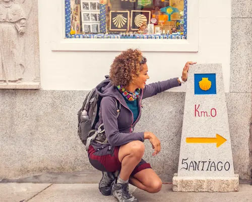 Woman kneeling next to Camino de Santiago stone sign